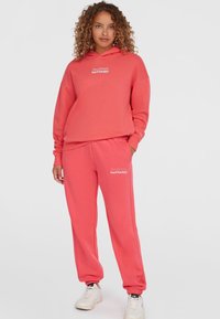 Korallenfarbene Kapuzenjacke und Jogginghose, aus einem Baumwollgemisch, mit lässigem Schnitt, gerippten Bündchen und Logo-Stickerei auf beiden Teilen. Weiße Sneaker.