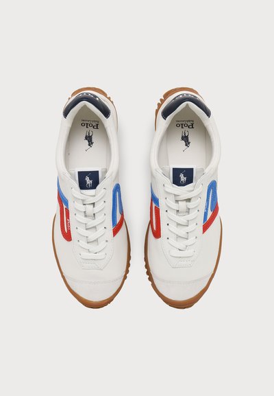 Ζευγάρι λευκά αθλητικά παπούτσια Polo Ralph Lauren με κόκκινες και μπλε ρίγες, λευκά κορδόνια, λαστιχένιες σόλες και λογότυπο στις εσώσολες και στις γλώσσες.