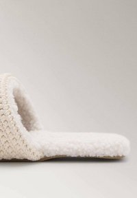 Pantofole beige da interno con una morbida tomaia testurizzata, apertura sul retro e una suola soffice e imbottita per il massimo comfort. Design minimalista.