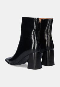 Botas de tobillo de cuero negro con un acabado brillante, puntera afilada y tacón cuadrado grueso. Cierre lateral con cremallera para un fácil uso.