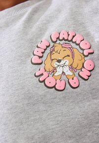 Szary bawełniany sweatshirt z kolorową grafiką Skye z Paw Patrol, z różowymi akcentami i zabawnym letteringiem otaczającym wzór.