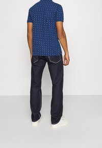 T-paita tummansinisellä värillä, valkoisella sydänkuvioinnilla, lyhyillä hihoilla. Yhdistetty tummiin farkkuihin ja valkoisiin lenkkareihin, nähtynä takaa.