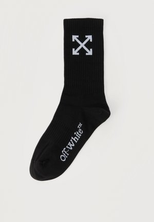 Chaussette unie noire avec logo Off-White™ blanc sur le pied et graphique d'arrows blanches entrecroisées près du haut.