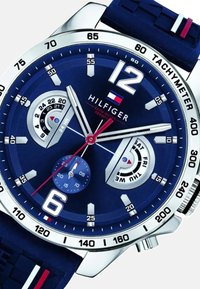 Orologio blu navy con cassa in acciaio inossidabile, dettagli in argento, due sottoquadranti, indicatori delle ore bianchi, tachimetro e cinturino in gomma testurizzata.