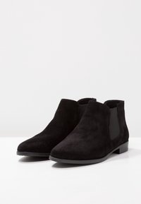 Stivaletti neri in suede con pannelli laterali elasticizzati e tacco basso, caratterizzati da una texture liscia e una forma moderna e slanciata.