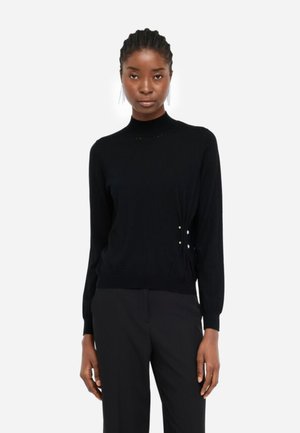 Maglione nero con colletto alto, maniche lunghe e bottoni decorativi sul lato. Realizzato in tessuto morbido con una trama liscia.