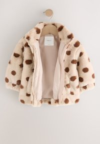 Veste en fausse fourrure avec une base beige et de grands pois marron, dotée d'une fermeture éclair à l'avant et d'une texture douce et moelleuse. Intérieur doublé de tissu rose clair.
