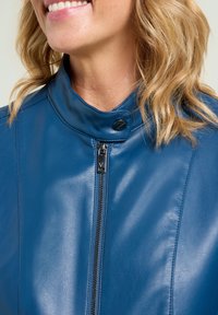 Blauwe leren jas met een hoge kraag, voorzien van een rits aan de voorkant en drukknopen. Gladde textuur met een aansluitend ontwerp.