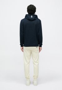 Felpa con cappuccio blu navy con logo sulla schiena e pantaloni sportivi color avorio. Tessuto morbido con polsini e orlo a coste, abbinata a sneaker bianche.