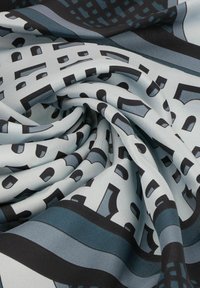 Zijden sjaal met een gladde textuur, voorzien van een geometrisch patroon in zwart en verschillende tinten blauw op een lichtgrijze achtergrond.