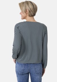 Langarmshirt in Marineblau mit einem weißen geometrischen Muster. Weicher Stoff, runder Ausschnitt und lockere Passform. Kombiniert mit blauen Jeans.