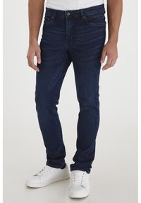 Mörkblå denimjeans med slim fit, med en klassisk design med fem fickor och lätt blekning längs låren. Bärs med vita sneakers.