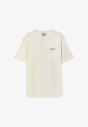 Beżowy bawełniany t-shirt z krótkimi rękawami. Na lewej piersi znajduje się napis „SURF INC.” oraz grafika fali w kolorach fioletowym i czerwonym. Okrągły dekolt.