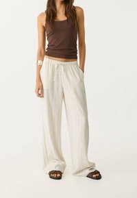 Débardeur marron associé à un pantalon ample à rayures beige clair. Le pantalon comporte une taille froncée avec cordon de serrage et des poches latérales. Sandales marron.