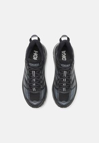Chaussures de sport noires et grises avec empeigne en mesh, bout rond et semelle en caoutchouc épaisse. Présente des lacets blancs et un logo de marque sur la languette.
