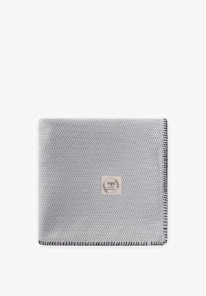 Couverture tissée bleu clair et blanche avec un motif en chevron, des bords sombres cousus, et une étiquette de marque "cigit" centrée.