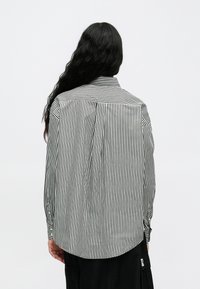 Gestreiftes schwarz-weißes Langarmhemd mit kragenförmigem Ausschnitt, Knopfmanschetten und einem leicht abgerundeten Saum auf der Rückseite.