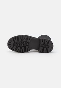 Suola nera delle scarpe con un motivo di battistrada robusto, caratterizzato da scanalature profonde e bordi arrotondati per una migliore aderenza. Realizzata in materiale gommoso resistente.