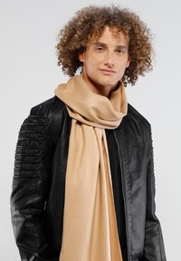 Bufanda beige hecha de una tela suave, colocada alrededor del cuello, combinada con una chaqueta de cuero negra con acentos acanalados en las mangas.