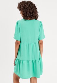 Robe vert menthe avec des manches courtes, design à volants, texture douce et coupe décontractée. Comprend un léger volant au bas.