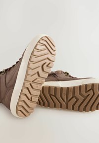 Braune Leder-Sneaker mit strukturierten Oberflächen, weißen Gummisohlen mit einem Zickzack-Profil und Metallösen für die Schnürsenkel.