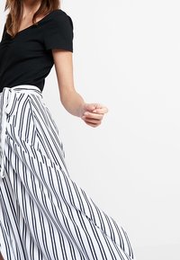 Black ribbed top paired with a white and navy striped wrap skirt, featuring a tie waist and flowing fabric.