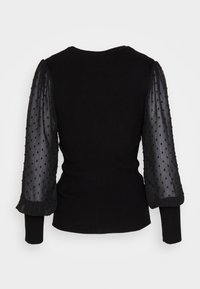 Top nero a maglia con maniche lunghe testurizzate in tessuto trasparente con un motivo a pois. Corpo a coste e scollatura rotonda.