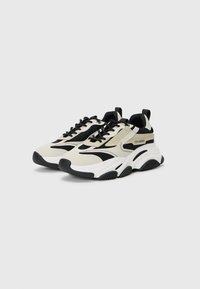 Chunky sneakers in cream and black, featuring mesh panels, lace-up design, padded collar, and textured rubber outsole.