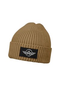 Tan knitted beanie with a ribbed texture. Features a black fabric patch displaying a silver star and wing design.
