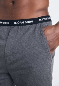 Szürke pamut rövidnadrág fekete elasztikus derékkal, rajta a "BJÖRN BORG" logóval. Oldalsó zsebekkel és sima textúrával rendelkezik.
