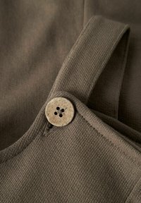 Tissu côtelé brun avec une large sangle et un bouton en bois circulaire à quatre trous. La texture est douce et légèrement extensible.