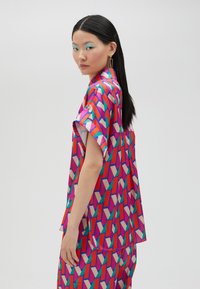 Short-sleeve shirt in vibrant geometric pattern with pink, red, green, and beige colors; silky texture and relaxed fit.
