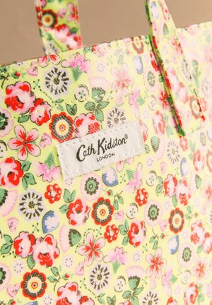 Virágmintás sárga táska piros, rózsaszín, zöld virágokkal, fehér, téglalap alakú Cath Kidston London felirattal a felső szélénél, fogantyúval látható.