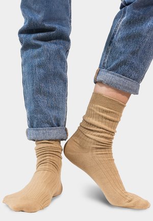 Beżowe skarpetki w rybkę z podwiniętym mankietem, noszone z podwiniętymi niebieskimi dżinsami. Skarpetki charakteryzują się miękką teksturą i dopasowanym krojem.