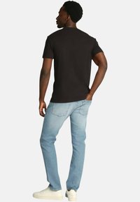 T-shirt nera a maniche corte abbinata a jeans in denim azzurro chiaro, che mostra un design aderente e uno stile minimalista, indossata con sneaker bianche.