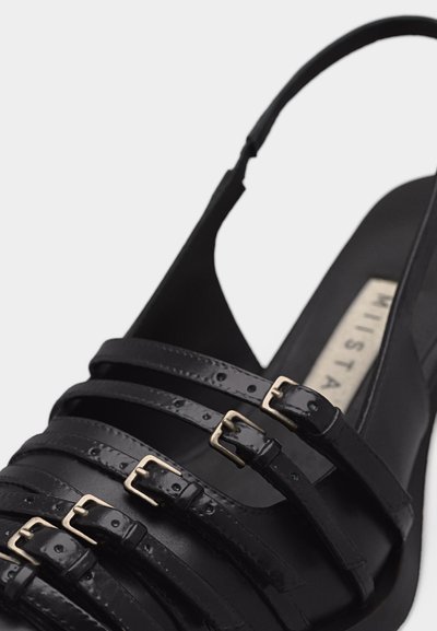 Μαύρο σανδάλι με λουράκια, πέντε ρυθμιζόμενες αγκράφες και τακούνι τύπου slingback σε φωτεινό φόντο.
