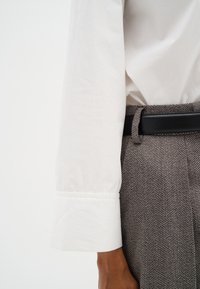 Witte shirt met opgerolde mouwen en grijze herringbone broek, met een zwarte leren riem. Close-up van bovenkleding en patronen.