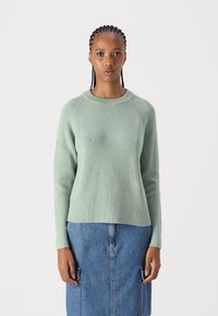 Hellgrüner gerippter Pullover mit rundem Halsausschnitt und langen Ärmeln, kombiniert mit einem Jeansrock mit Fronttaschen.