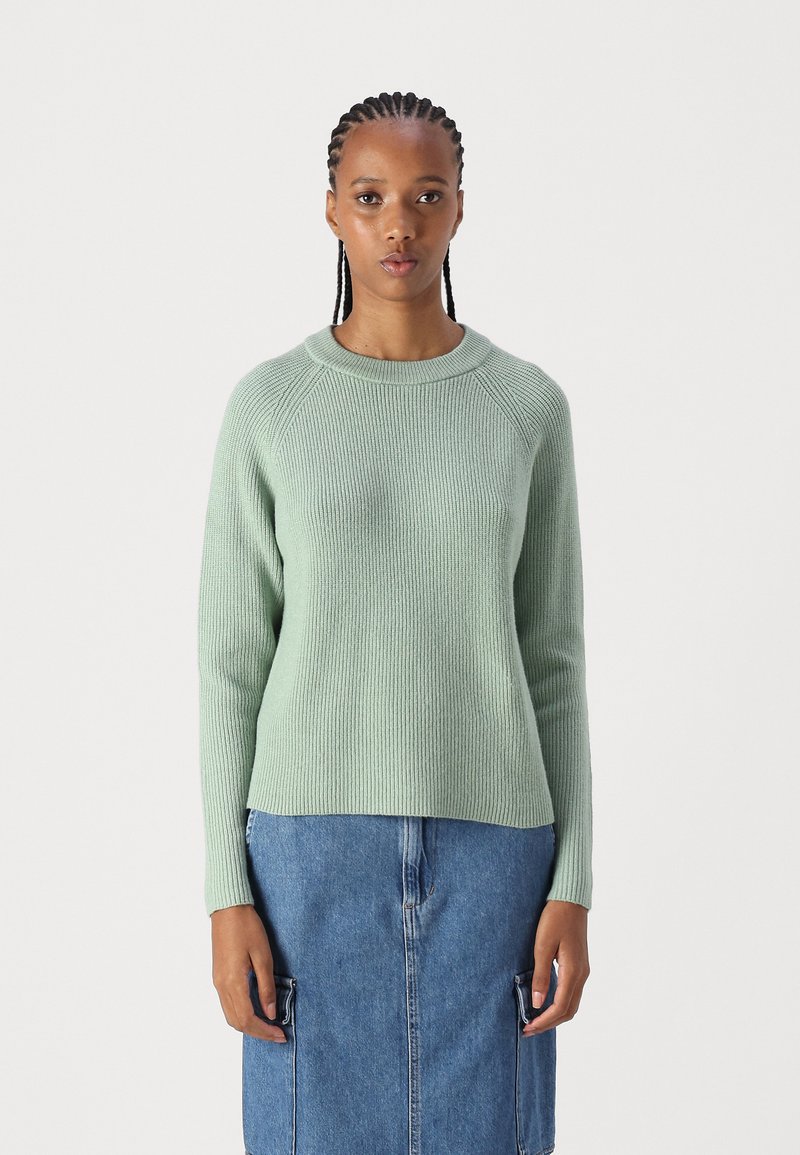 Hellgrüner gerippter Pullover mit rundem Halsausschnitt und langen Ärmeln, kombiniert mit einem Jeansrock mit Fronttaschen.
