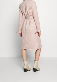 Světle růžový semišový trenčkot s páskem v pase, bočními rozparky a ohrnutými rukávy. Kombinovaný s embosovanými béžovými kotníkovými botami a černými lodičkami.