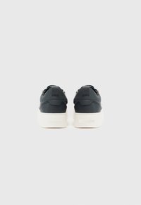 Schwarze Sneaker mit oberem Teil aus strukturiertem Leder, weißer Gummisohle, kurzem Fersenstück und silbernen Hardwaredetails. Minimalistisches Design mit klaren Linien.