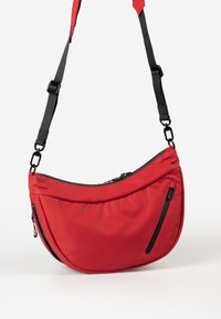 Borsa a spalla in tessuto rosso con forma curva, dettagli in cerniera nera, tracolla regolabile e due tasche con cerniera sul fronte.
