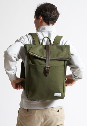 Grüner Canvas-Rucksack mit Rolltop-Design, braunem Lederriemen und Reißverschluss, Fronttasche und verstellbaren Schultergurten.