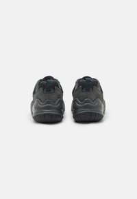 Par de zapatillas deportivas negras y gris oscuro vistas desde la parte trasera, con suelas texturizadas y tiradores, sobre un fondo blanco.