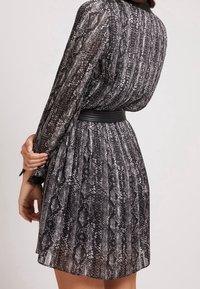 Krátké, plisované šaty s černo-bílým hadím vzorem, průhlednou tkaninou, dlouhými rukávy a černým páskem zvýrazňujícím pas.