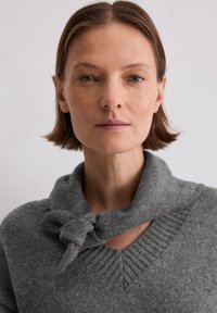 Grau gestrickter Pullover mit V-Ausschnitt und einem Knoten-Schal-Detail. Texturiertes Gewebe mit gerippten Akzenten am Ausschnitt.