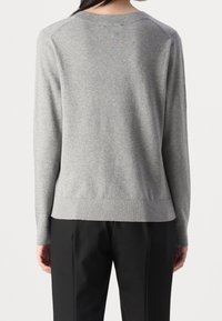 Pull en maille gris clair à coupe décontractée, avec un col et un ourlet côtelés, et des manches longues, associé à un pantalon noir. Texture lisse.