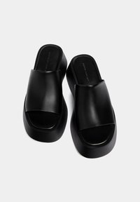 Zoccoli neri in pelle con fasce larghe, suole piatte e una finitura liscia. Presentano una punta quadrata e un design minimalista.