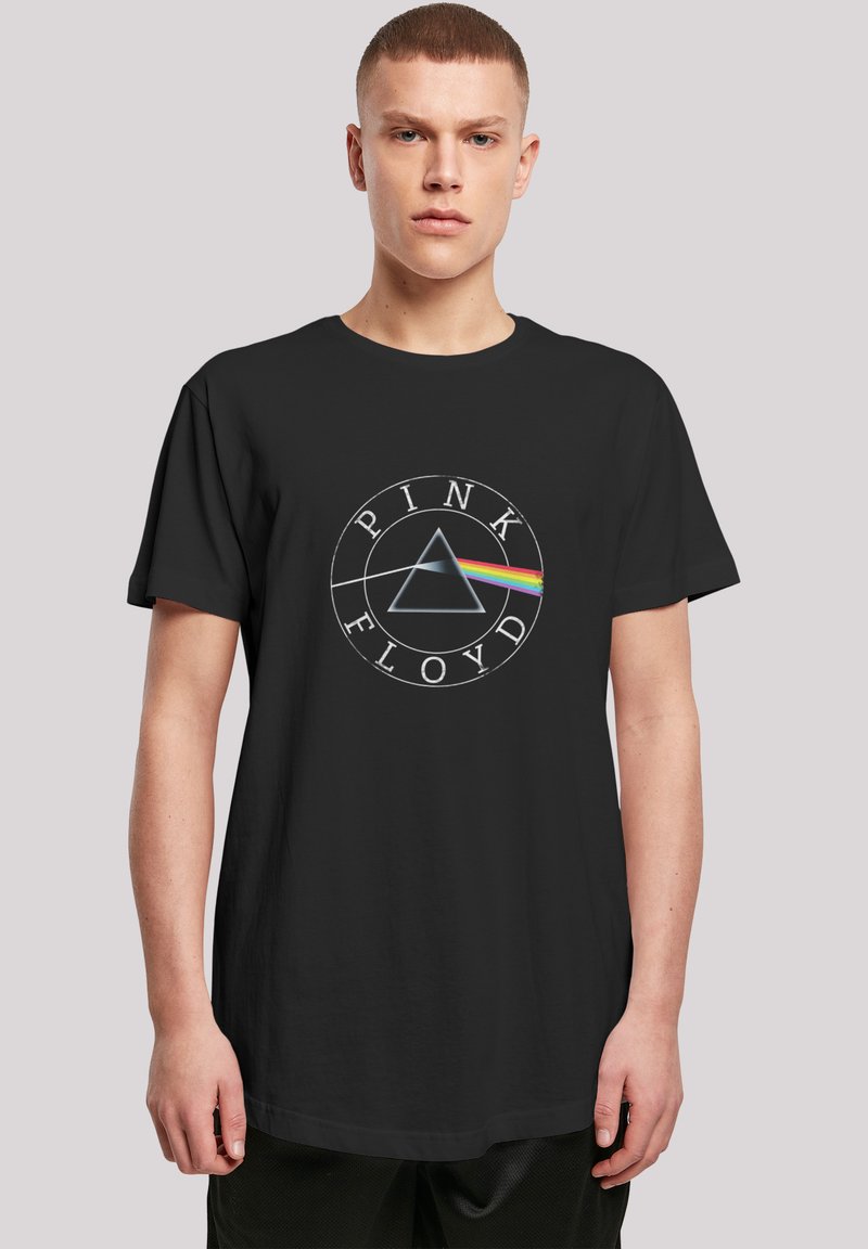 T-shirt noir présentant un graphique circulaire avec le texte "PINK FLOYD" et un triangle central, accentué par une bande arc-en-ciel en bas.