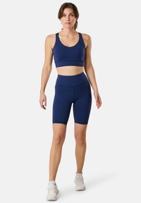 Marinblå sportbehå och matchande högmidjade cykelshorts, tillverkade av slätt, elastiskt tyg; minimal design med breda axelband och figurnära passform.
